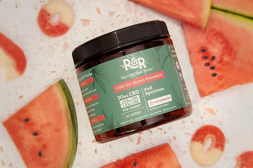 R&R watermelon-flavored CBD De-Stress gummies placed alongside freshly cut watermelons on a white stone